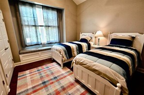 Ein Schlafzimmer mit zwei Betten, einem fensterbelaubten Fenster, einem Heizkörper und einem karierten Teppich.