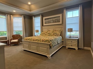 Une chambre avec un grand lit, deux tables de chevet, une chaise et une fenêtre avec des rideaux.
