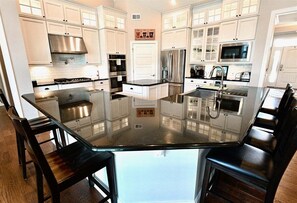 Una cocina moderna con armarios blancos, electrodomésticos de acero inoxidable e isla de vidrio con sillas.
