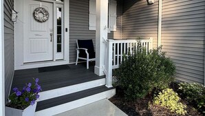 A porch with a white door, a bench, and a small garden area. - Coastal Club Beach House w/ Resort Style Amenities (Lewes)