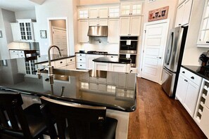 Una cocina moderna con armarios blancos, electrodomésticos de acero inoxidable y una isla central con taburetes de bar.