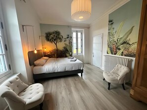 Ein Schlafzimmer mit Bett, zwei Stühlen, einem Heizkörper, einem Fenster und Wandbild.