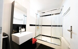 Ein modernes Badezimmer mit einem weißen Waschbecken, einem großen Spiegel und einer Duschkabine.