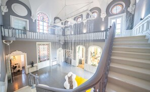 Ein großzügiger Innenraum mit einer imposanten Treppe, mehreren Bögen und einer hohen Decke.