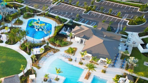 Eine Vogelperspektive eines Resorts mit einem großen zentralen Pool, mehreren Liegebereichen und einem Parkplatz.