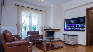 Een woonkamer met een open haard, leren banken, een glazen salontafel en een flatscreen-televisie waarop een streamingdienst wordt weergegeven.