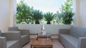 Een terras met rieten meubels, een houten tafel en twee planten in potten.