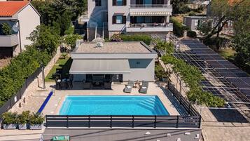 Un edificio moderno de dos pisos con piscina en la azotea, paneles solares y fachada de piedra.