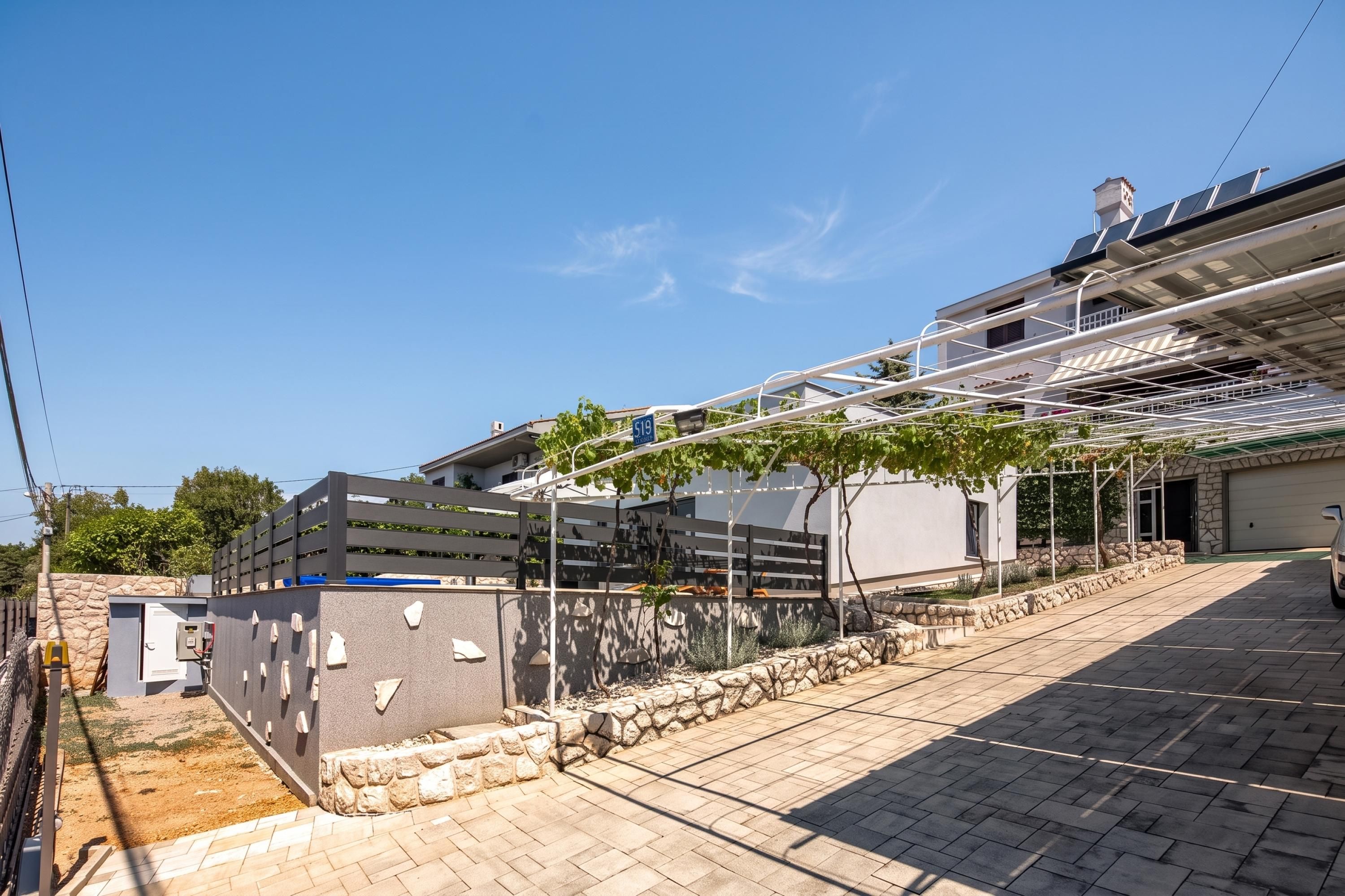 Un moderno edificio residencial con techo inclinado, paneles solares y un espacio al aire libre cubierto con un pérgola.