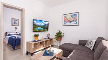 Un salón moderno con sofá, mesa de centro, televisor y cama con vistas al exterior.
