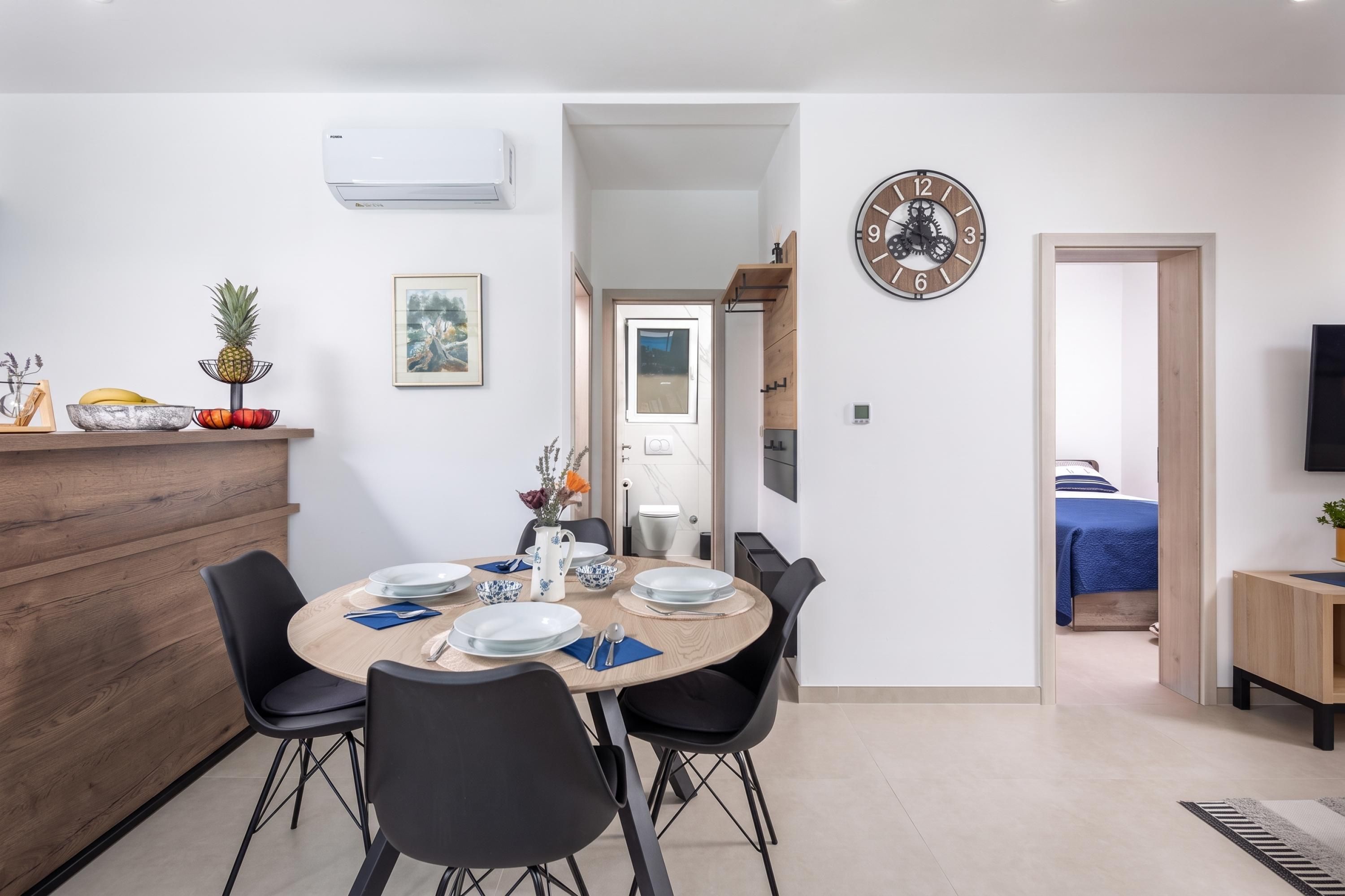 Un comedor moderno con una mesa redonda para cuatro, sillas negras y un equipo de aire acondicionado blanco en la parte superior.