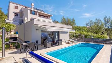 Una casa moderna de dos pisos con piscina, mobiliario exterior y zona de barbacoa.