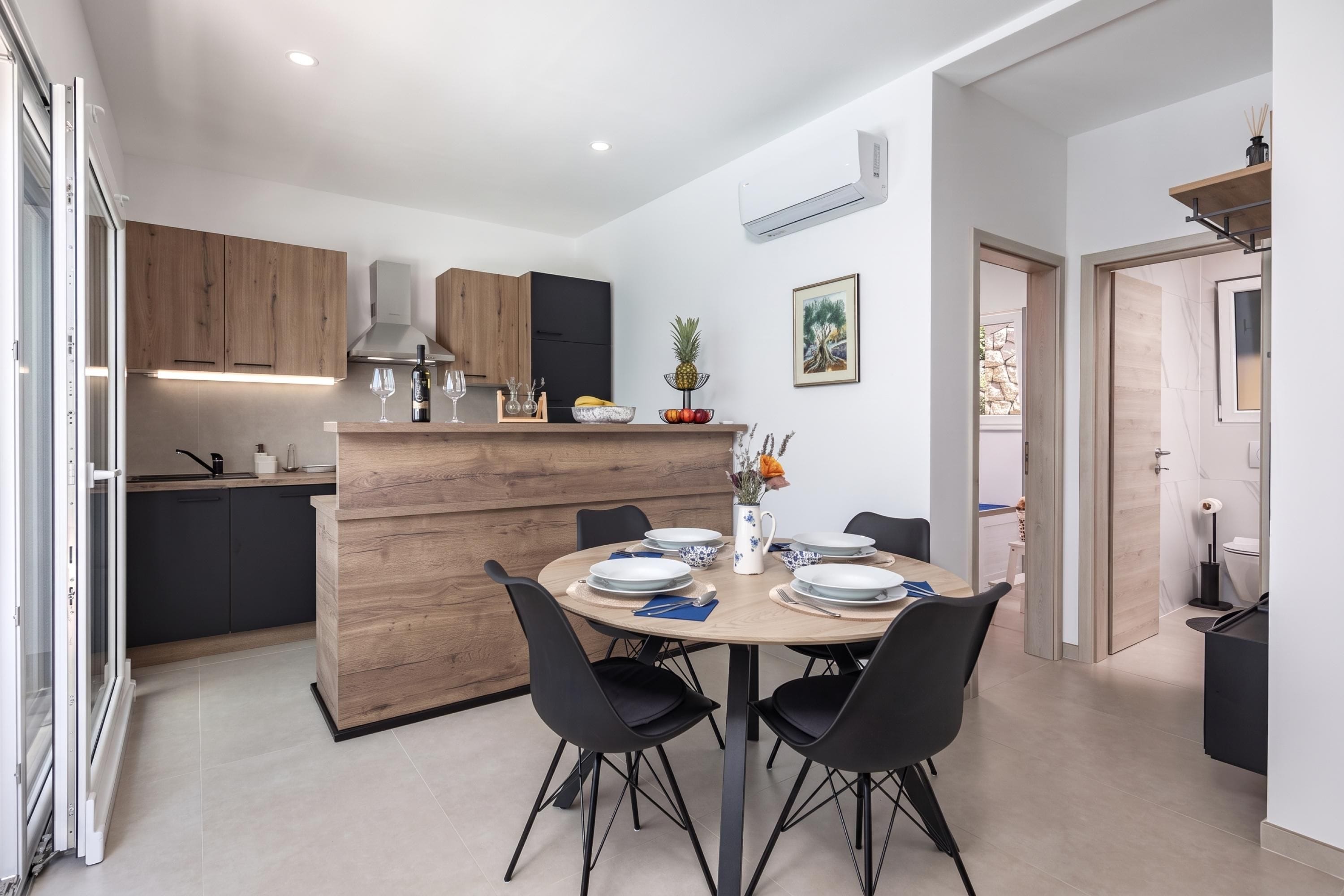 A modern kitchen with wooden cabinets, a central island, and a dining area with a round table and black chairs.