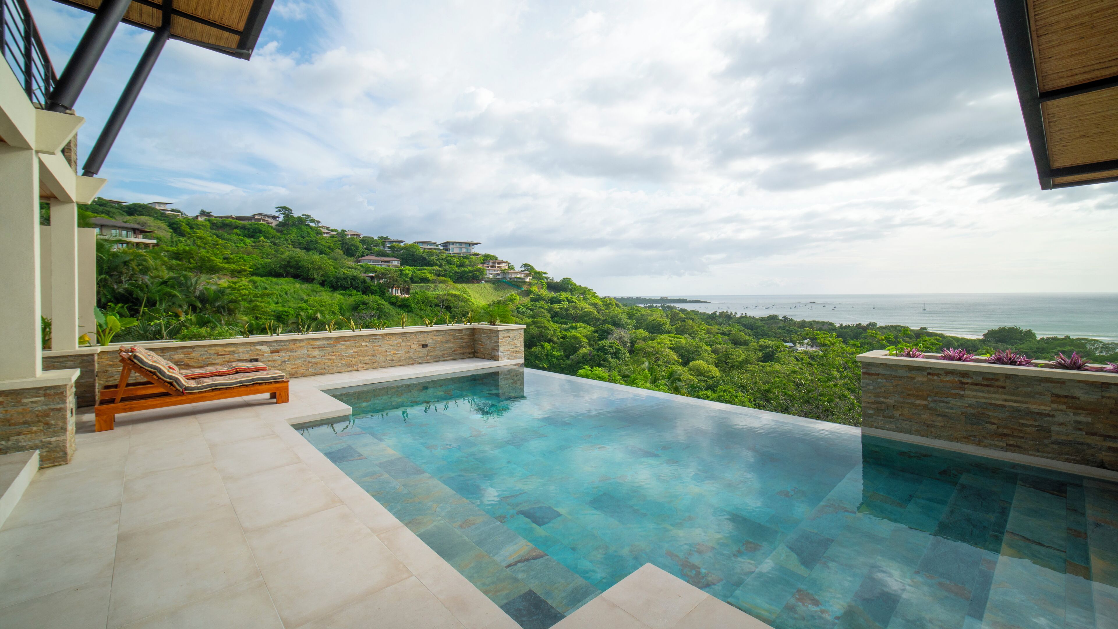 A infinity pool with a view of a coastal landscape and hillside residences.
