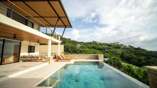 A modern outdoor swimming pool with a clear blue water surface, surrounded by a wooden deck and lounge chairs. - Ocean View Home sleeps 12 in Premier Gated Community (Tamarindo)