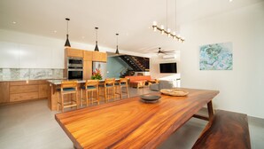 A modern kitchen with wooden cabinets, a dining area with a large wooden table, and a staircase leading to an upper level. - Ocean View Home sleeps 12 in Premier Gated Community (Tamarindo)