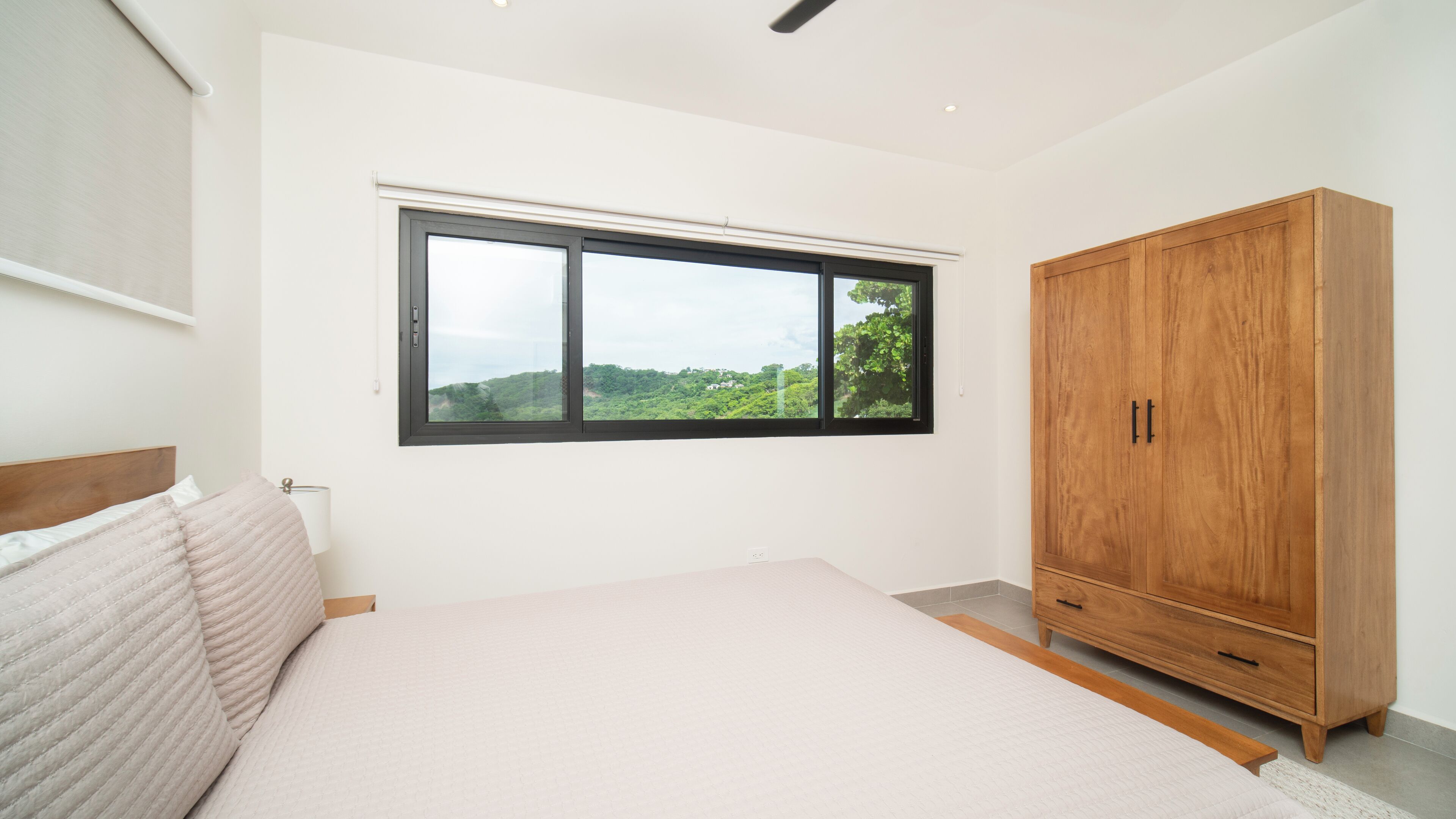 A bedroom with a large bed, a wardrobe, and a window with a view of greenery.