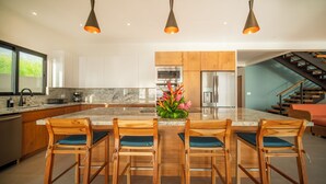 A modern kitchen with a central island, wooden chairs, and a decorative plant. - Ocean View Home sleeps 12 in Premier Gated Community (Tamarindo)