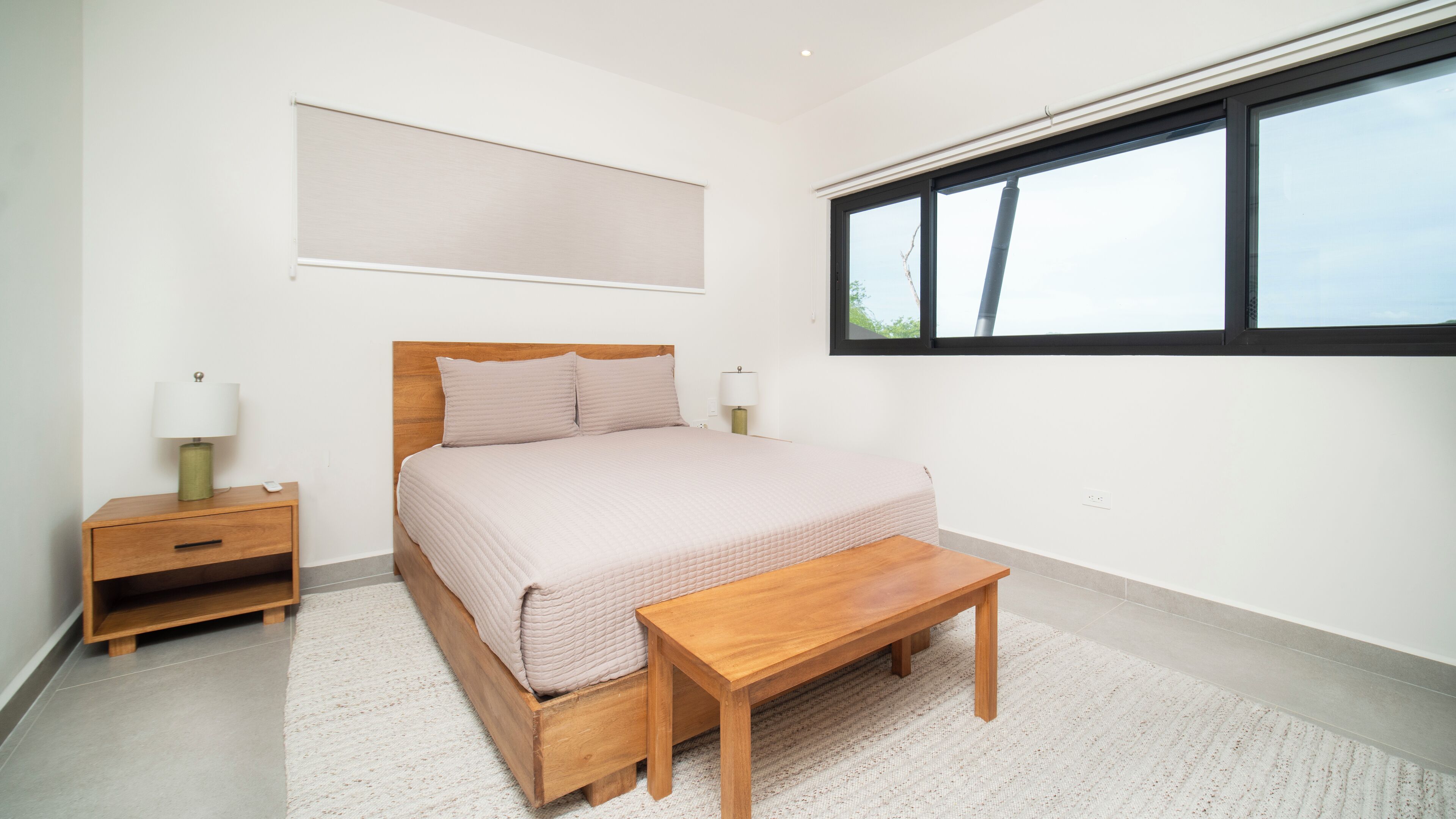 Une chambre à coucher comprenant un lit, des tables de chevet, un banc, une fenêtre et un luminaire fixé au mur.