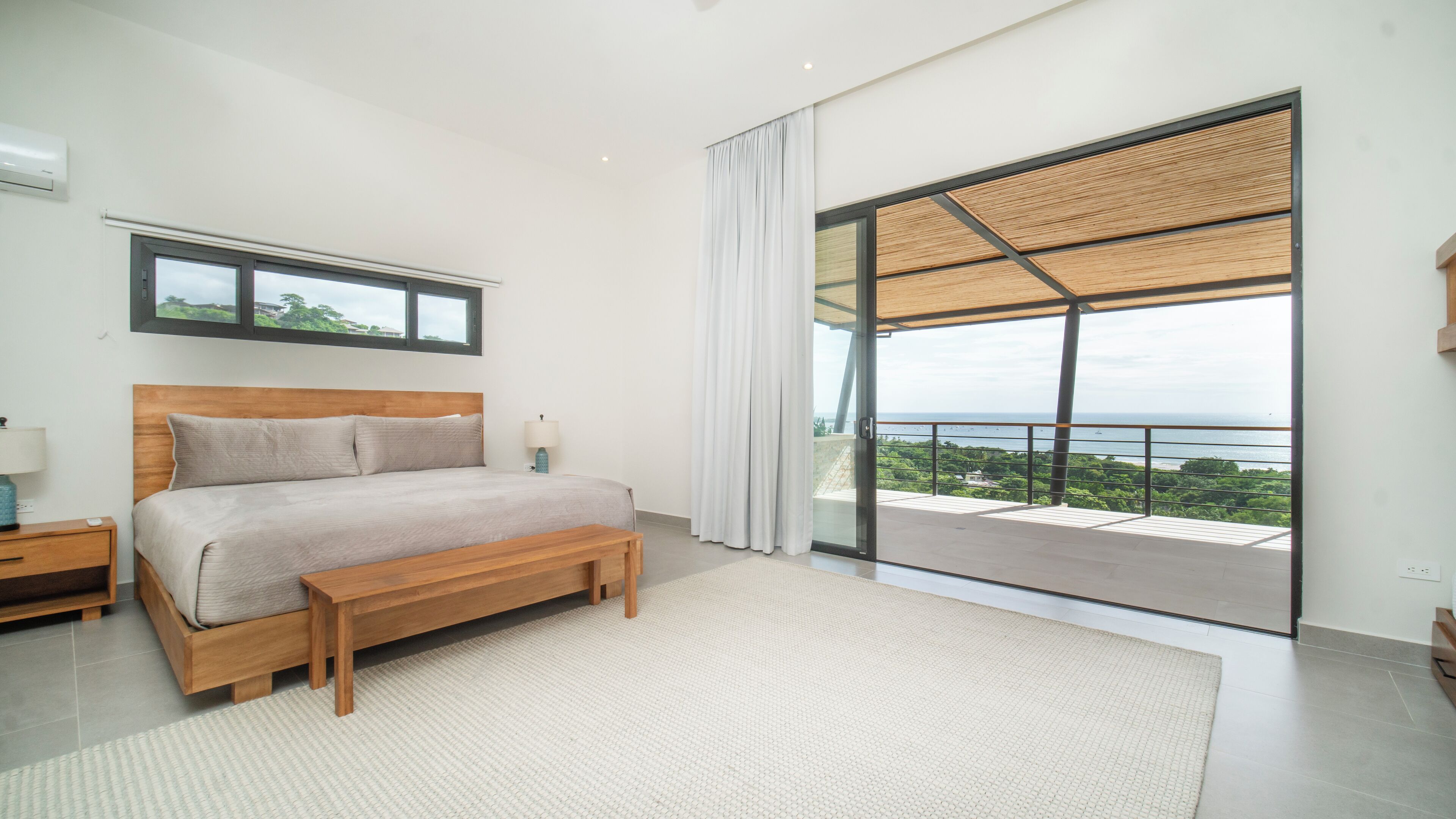 Een slaapkamer met een groot bed, nachtkastje, een bankje, een raam en uitzicht op zee.