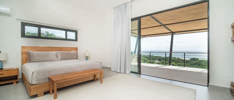 Een slaapkamer met een groot bed, nachtkastje, een bankje, een raam en uitzicht op zee.