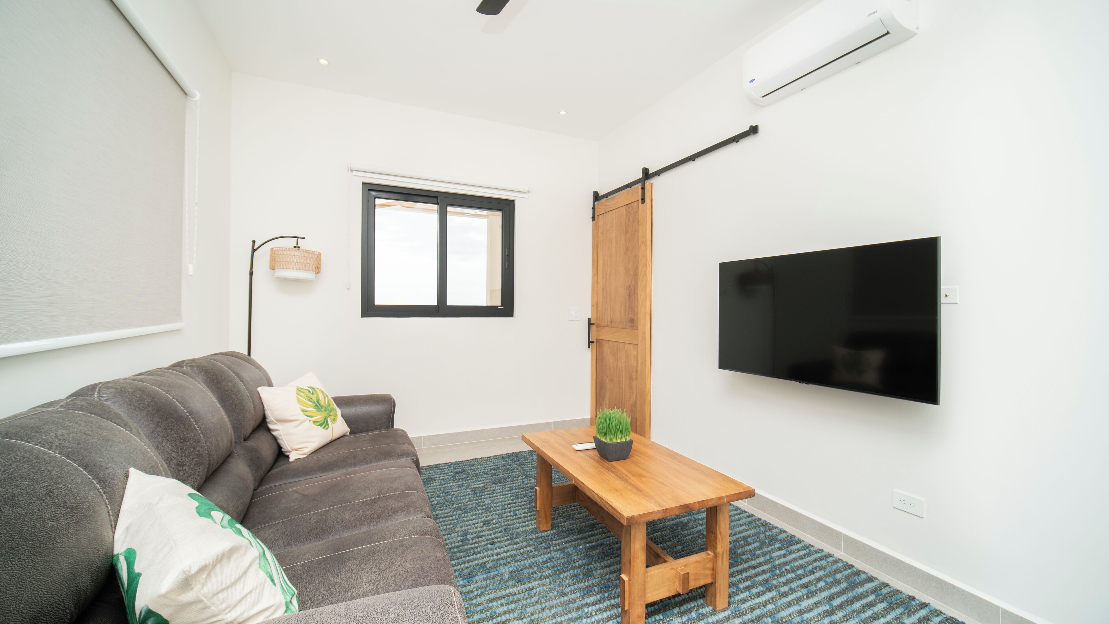 Uma sala de estar moderna com um sofá, uma mesa de centro, uma televisão e uma porta de correr.