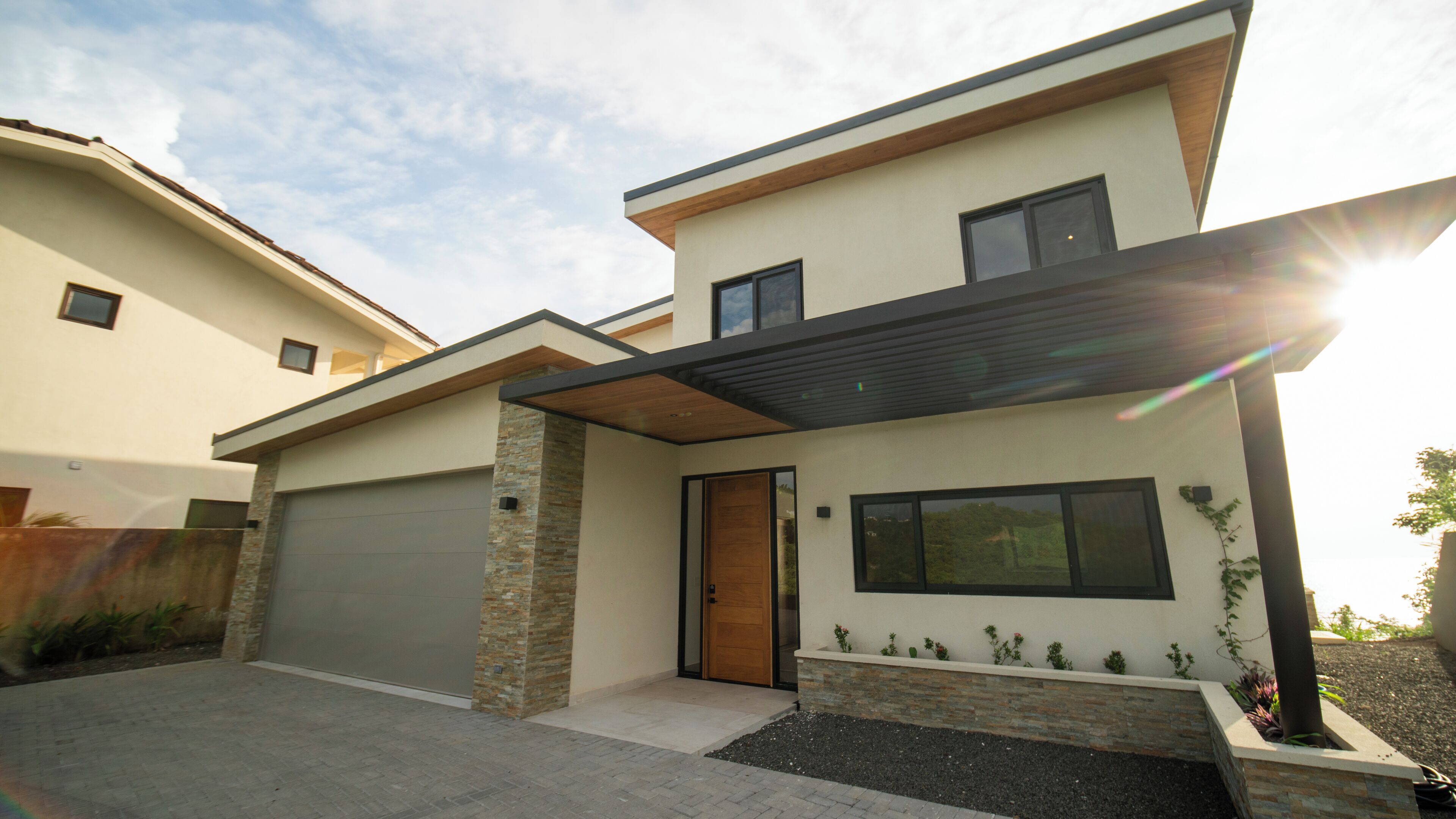 Une maison moderne à deux étages, dotée d’un garage, d’une porte d’entrée en bois et d’une grande fenêtre.