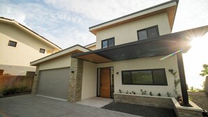 A modern two-story house with a garage, a wooden front door, and a large window. - Ocean View Home sleeps 12 in Premier Gated Community (Tamarindo)
