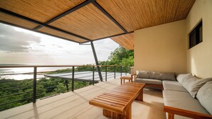 A modern balcony with a wooden table and sofa, overlooking a scenic landscape. - Ocean View Home sleeps 12 in Premier Gated Community (Tamarindo)