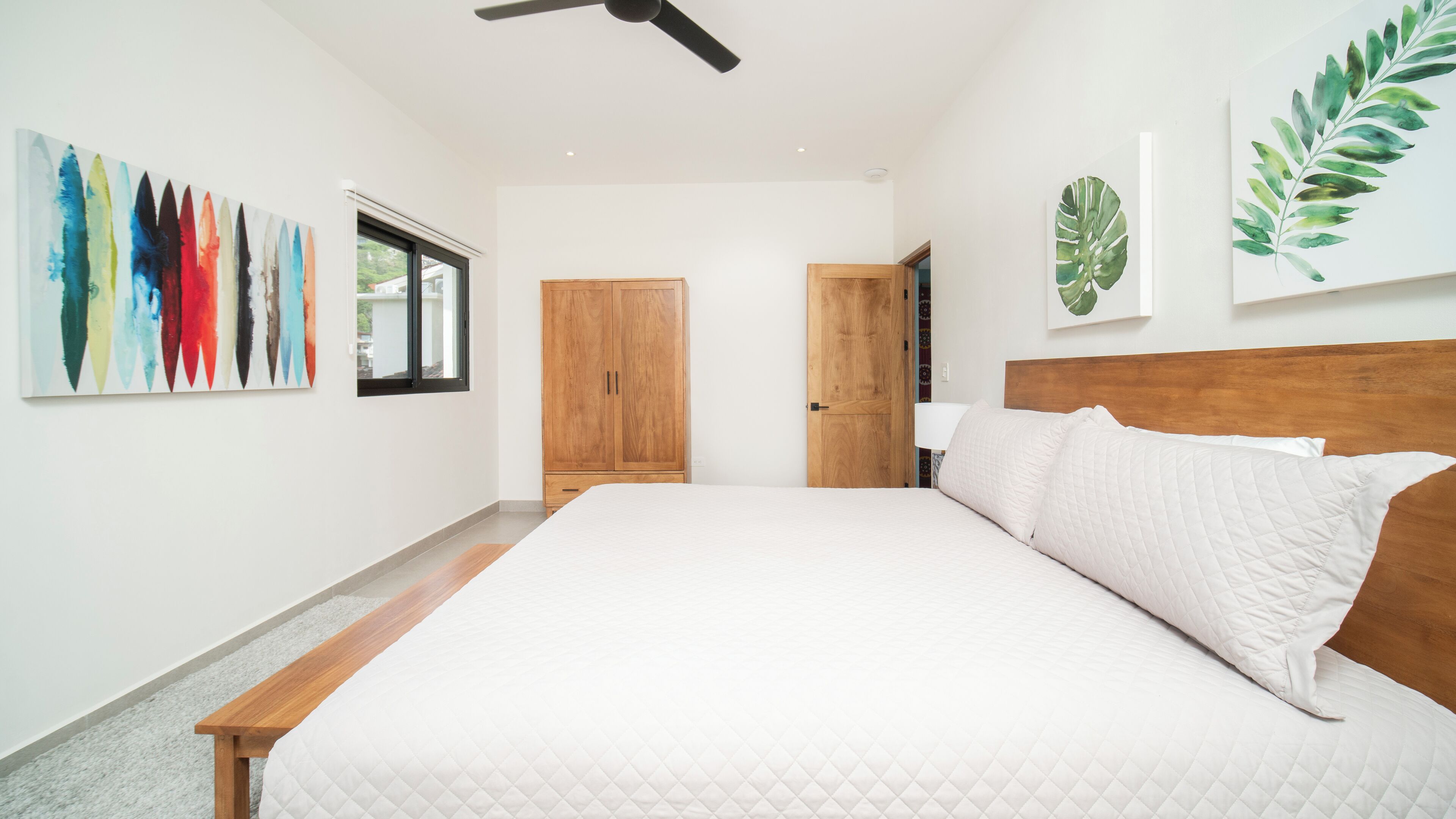 A bedroom with a large bed, wooden wardrobe, and a ceiling fan.