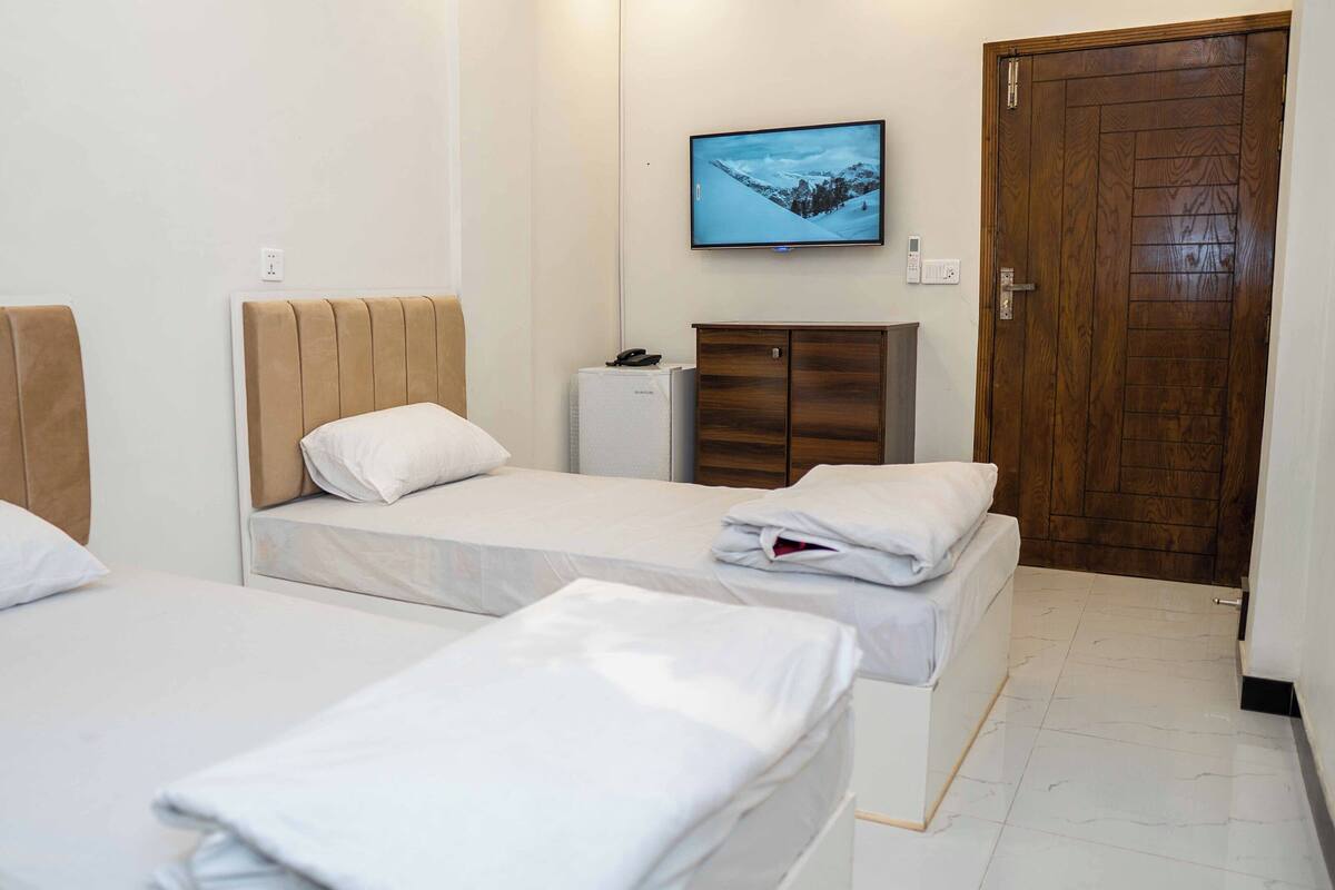 A hotel room with two beds, a wooden wardrobe, a small desk with a phone, and a TV on the wall.