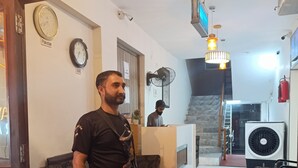 Un hombre de pie en un vestíbulo con sofás estampados, un reloj y un extintor.