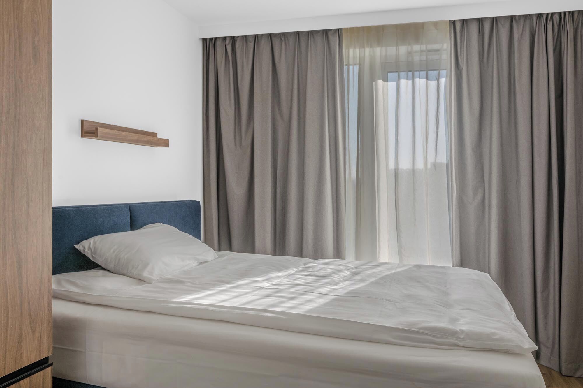 A bedroom with a bed, a headboard, and a window with curtains.