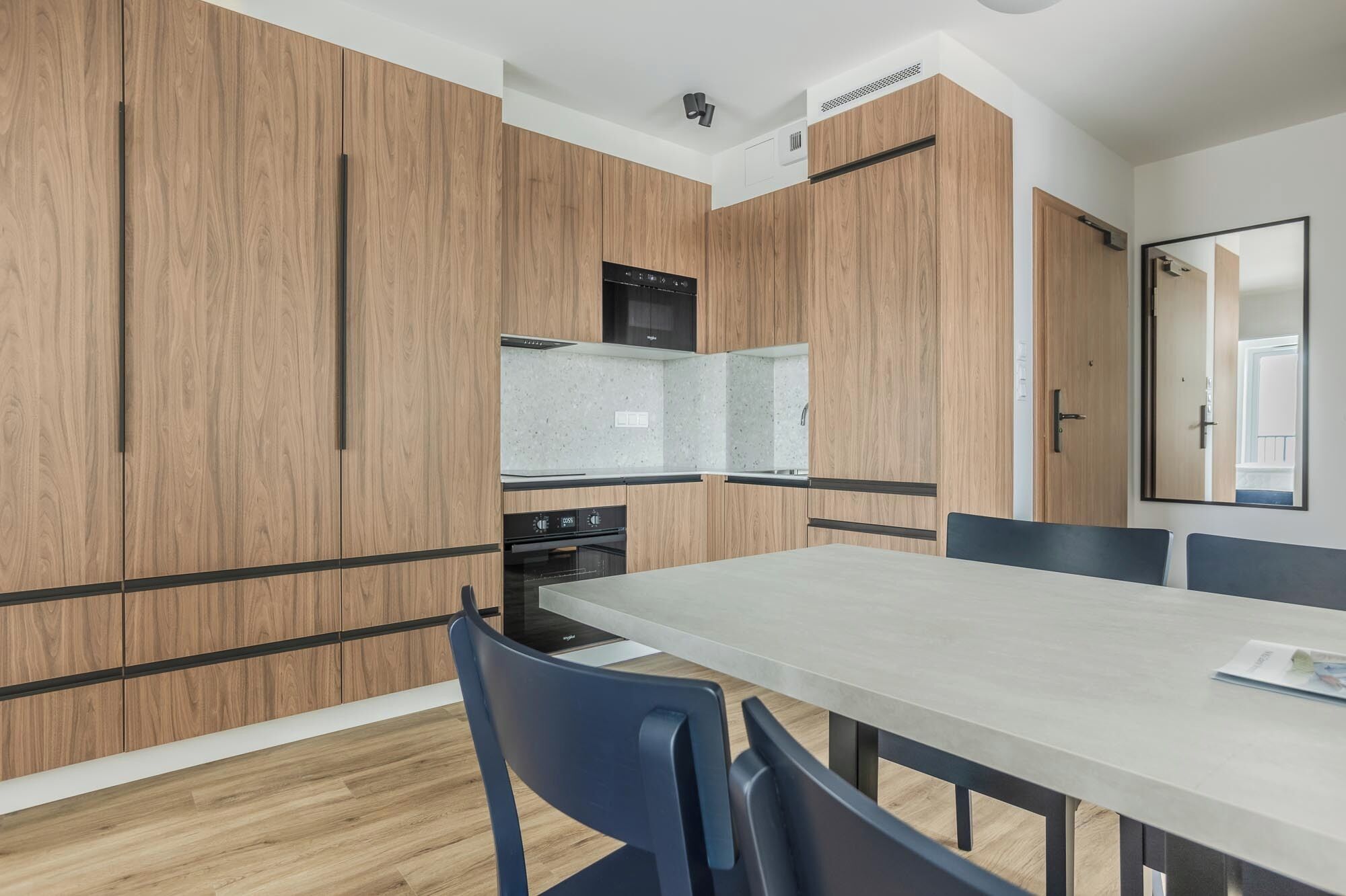 A modern kitchen with wooden cabinetry, a built-in oven, and a dining area with a table and chairs.