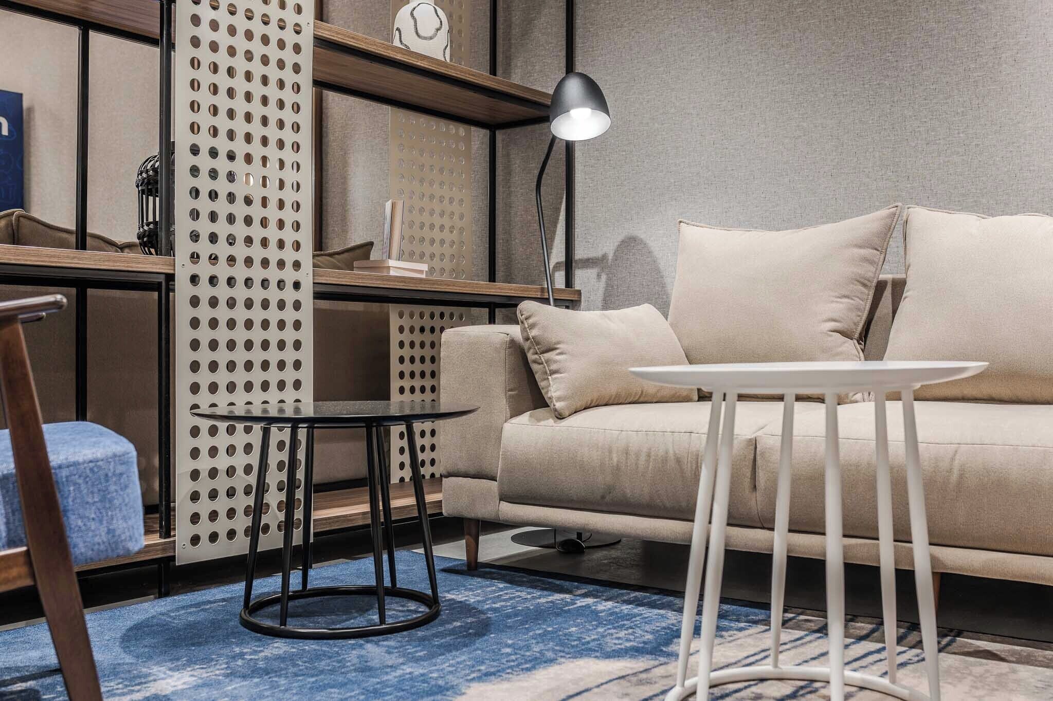 A modern living room with a beige sofa, a round white table, a black floor lamp, and a blue patterned rug.