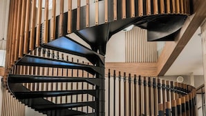 A spiral staircase with wooden and metal elements, a modern chandelier, and a view of the interior space.