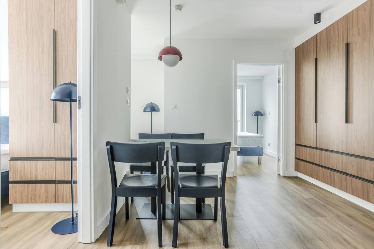 Een moderne eethoek met twee zwarte stoelen en een tafel, houten vloeren en een rode hanglamp.
