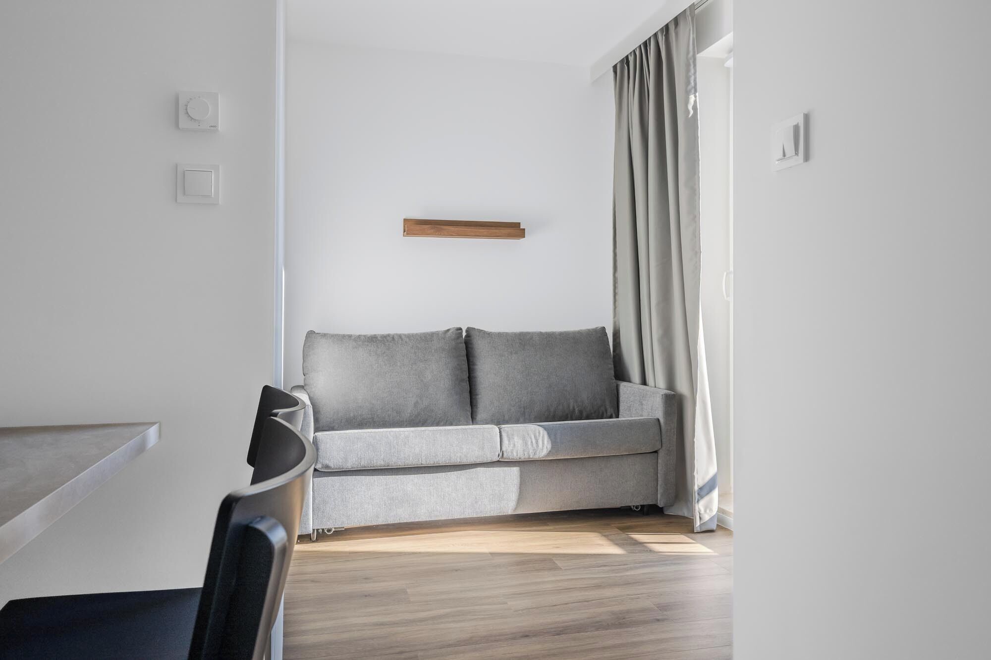 Un salon moderne avec un canapé gris, une étagère en bois et une chaise noire.