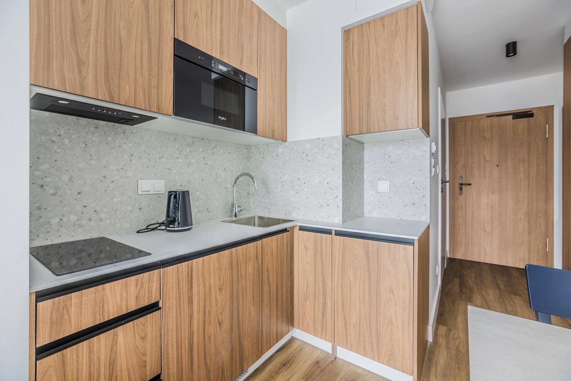 A compact kitchen with wooden cabinets, a built-in microwave, and a countertop with a kettle.