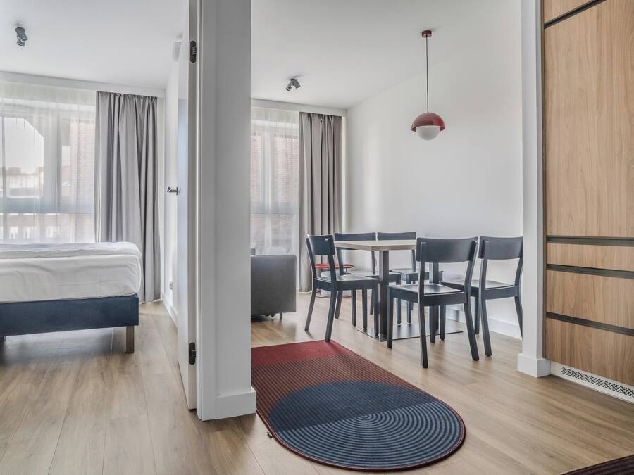 A modern hotel room with a bed, a desk, and a dining area.