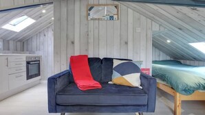 A compact room with a kitchenette on one side, a blue sofa with cushions, and a bed with a green blanket. - Light Bright Loft Studio with view of City & Canal (London)
