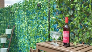 A bottle of wine and a glass on a wooden table against a green ivy wall. - Family Friendly Studio inc free Parking and Garden (London)