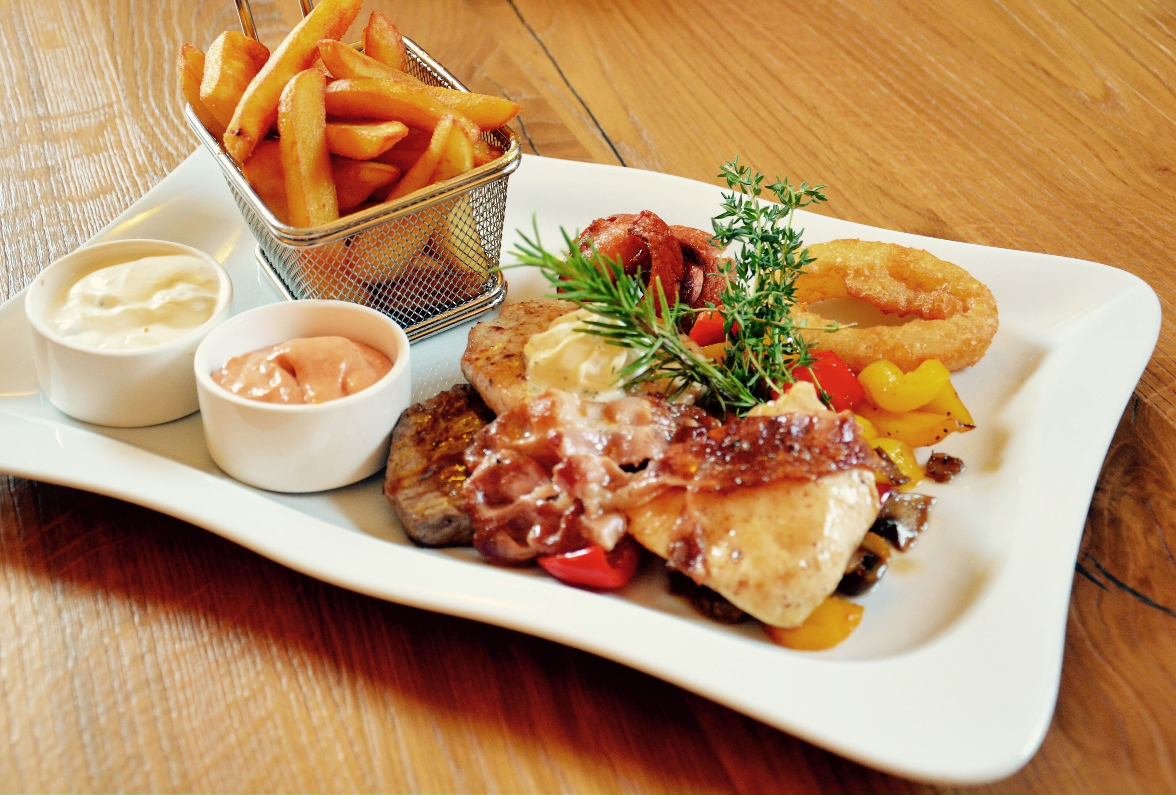 A plate of food including steak, fries, and onion rings, with two dipping sauces.