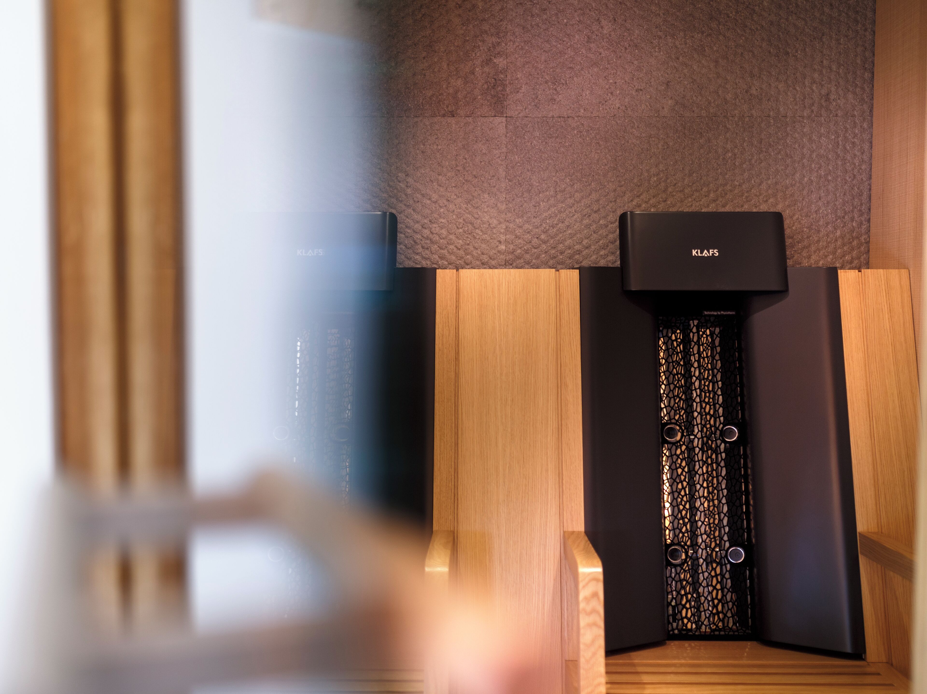 A modern, minimalist room with a wooden floor, a textured wall, and a black KLAFS appliance.