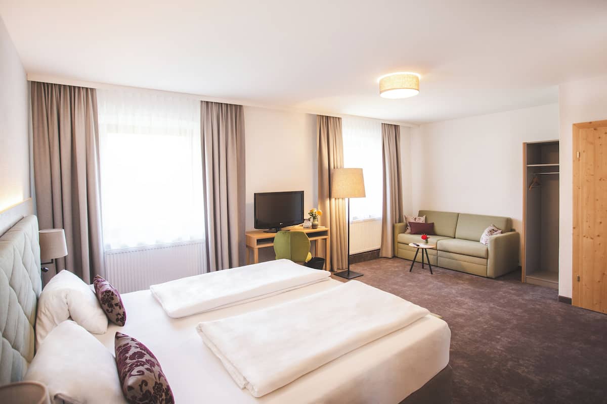 A hotel room with a bed, a desk, a television, a sofa, and a wardrobe.