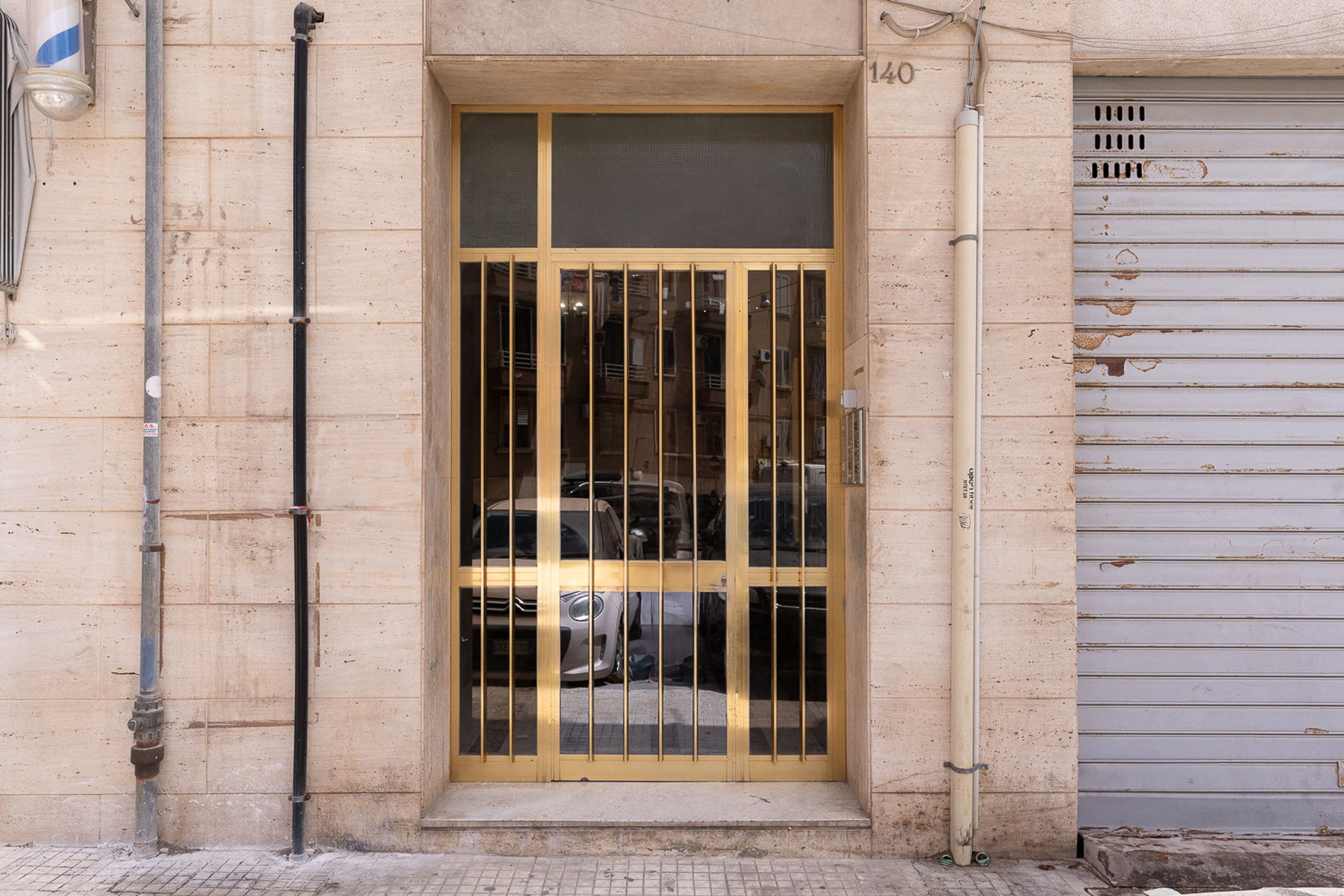 A building entrance with a metal gate, a number "140" above the door, and a garage door to the right.