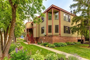 A two-story building with a brick foundation and a green facade, featuring a central staircase and a small front porch. - Moose Mgmt at Ski Team 1: Walk to PC Mtn Resort-Wood Burning Fireplace-Free Bus (Park City)