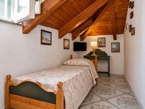 Ein Schlafzimmer mit Holzbalkendecke, einem Bett, einem Schreibtisch und einem Fernseher.