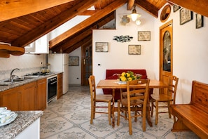 Cucina con mobili in legno, tavolo da pranzo con sedie, divano rosso e parete con quadri.