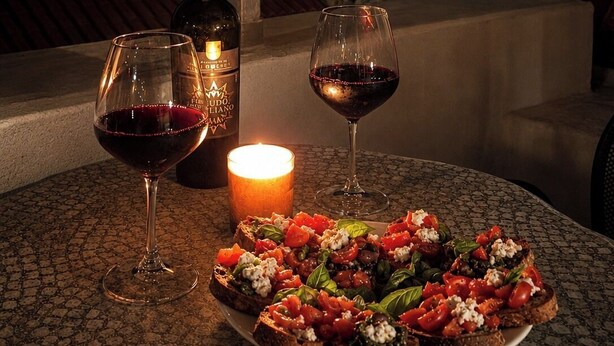 Ein Tisch mit einer Weinflasche, zwei Gläsern, einer Kerze und einer Portion Bruschetta.